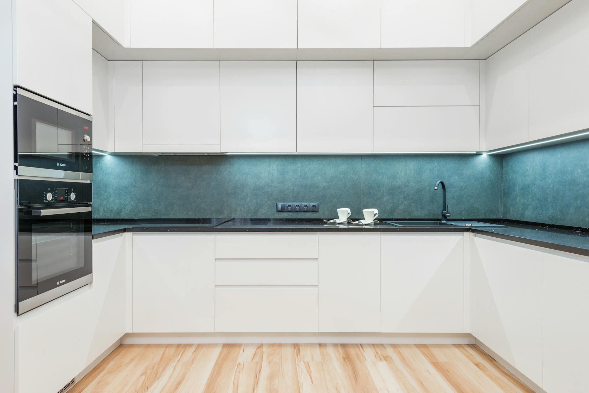 White kitchen with a teal backsplash and light wood-look flooring